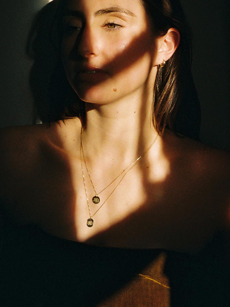 Woman in shadows with two faceted monogrammed necklaces
