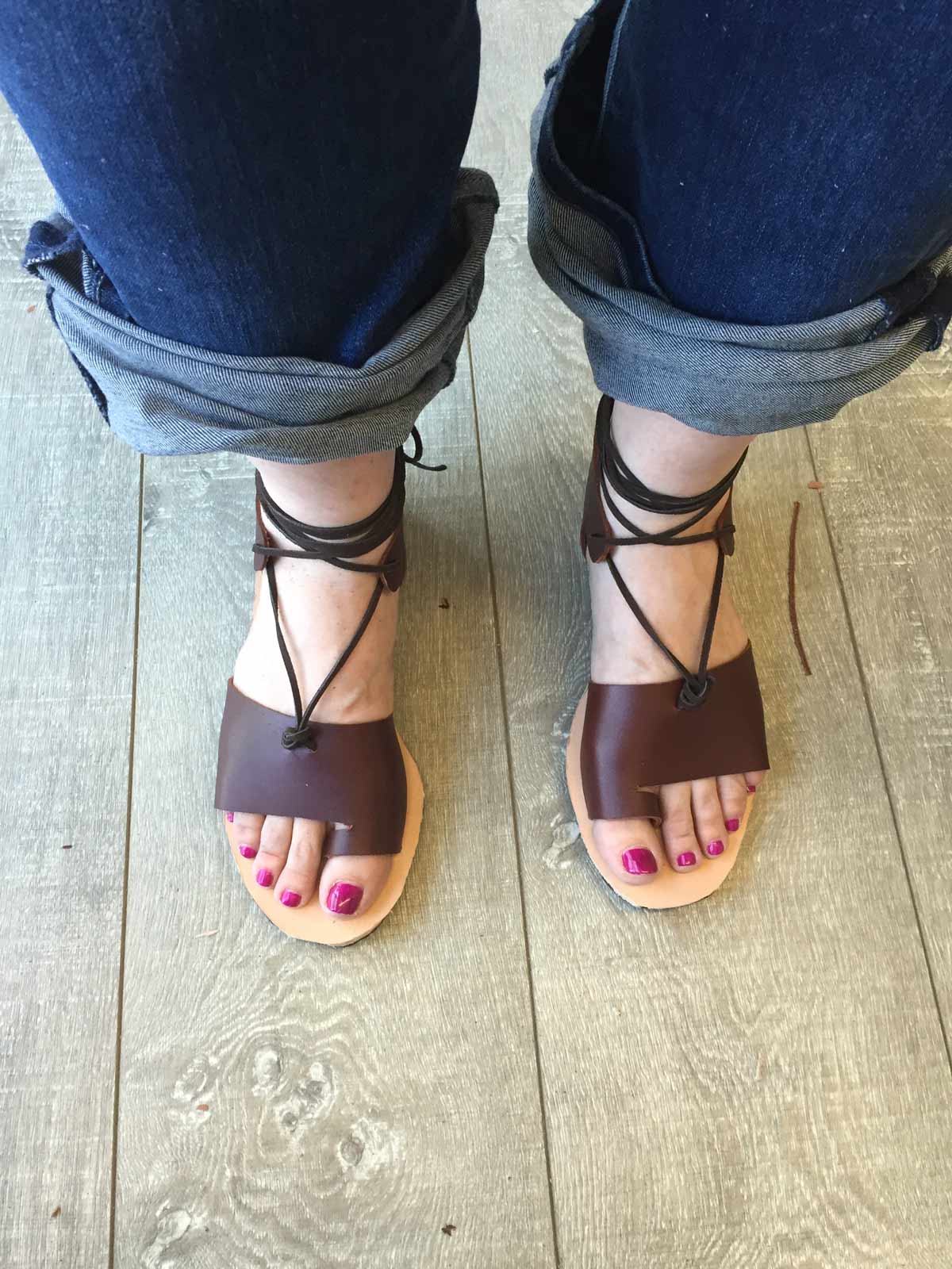 looking down at a pair of legs and feet in jeans and homemade brown leather sandals with red toenail polish
